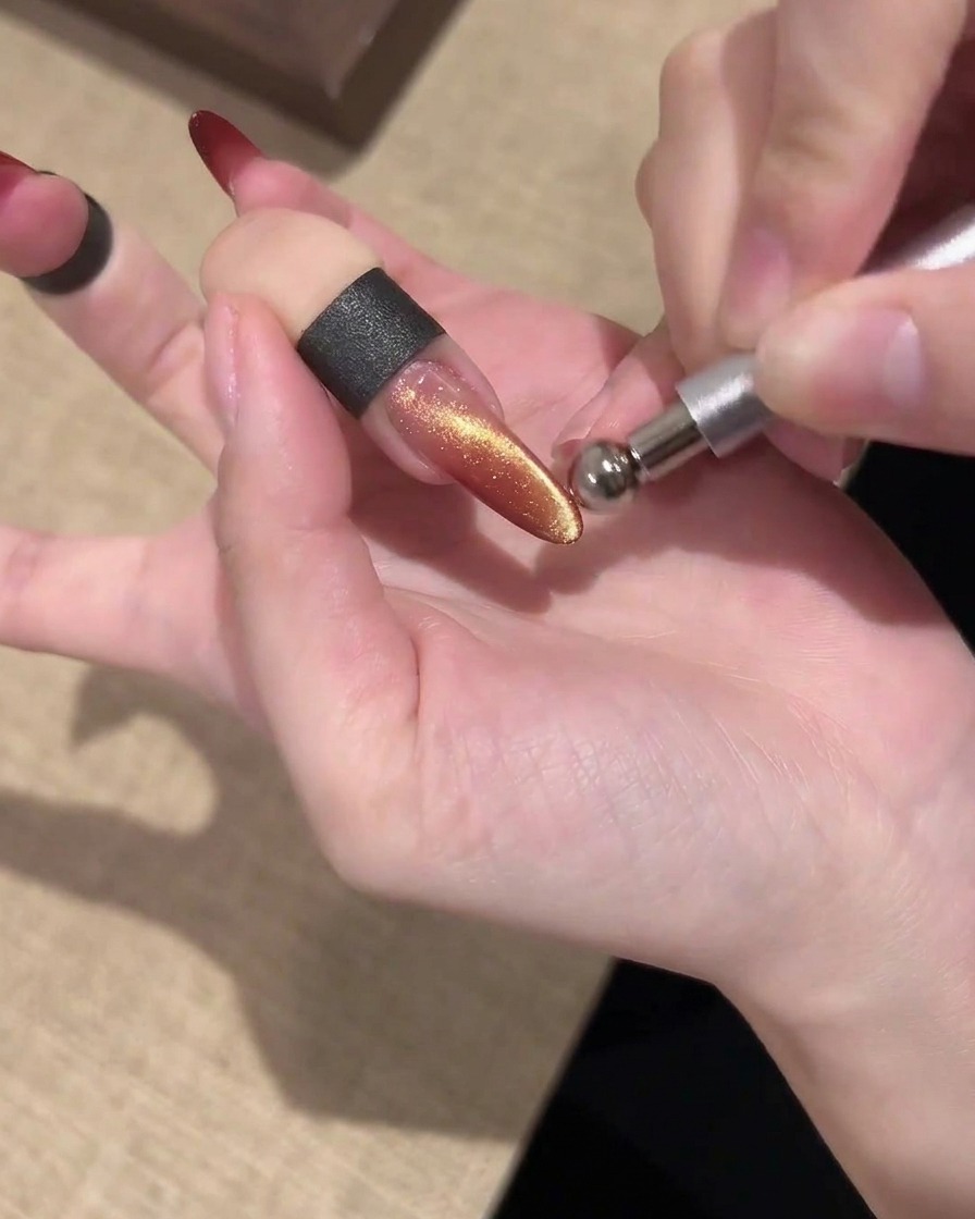 A bar magnet held parallel above a shimmering gold and red cat eye nail to shape the light.