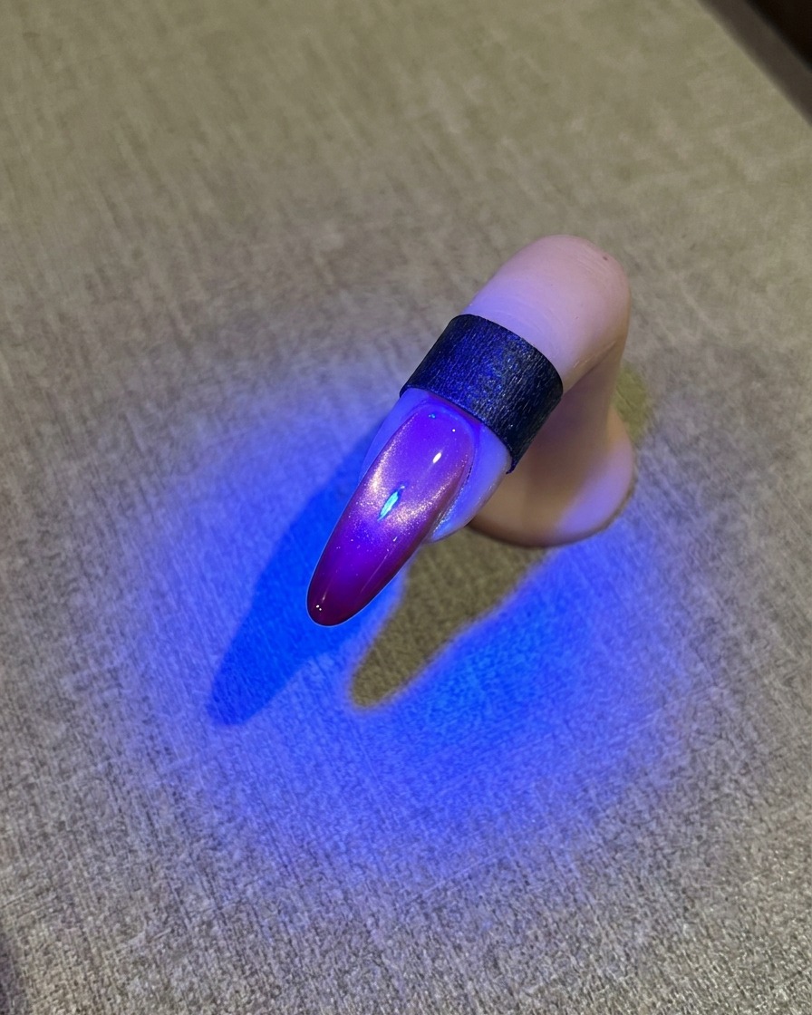 A nail under a blue UV lamp showing a glossy cat eye finish.