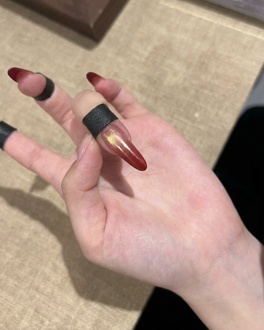 A finished red gradient cat eye nail with gold accents shown on a hand.