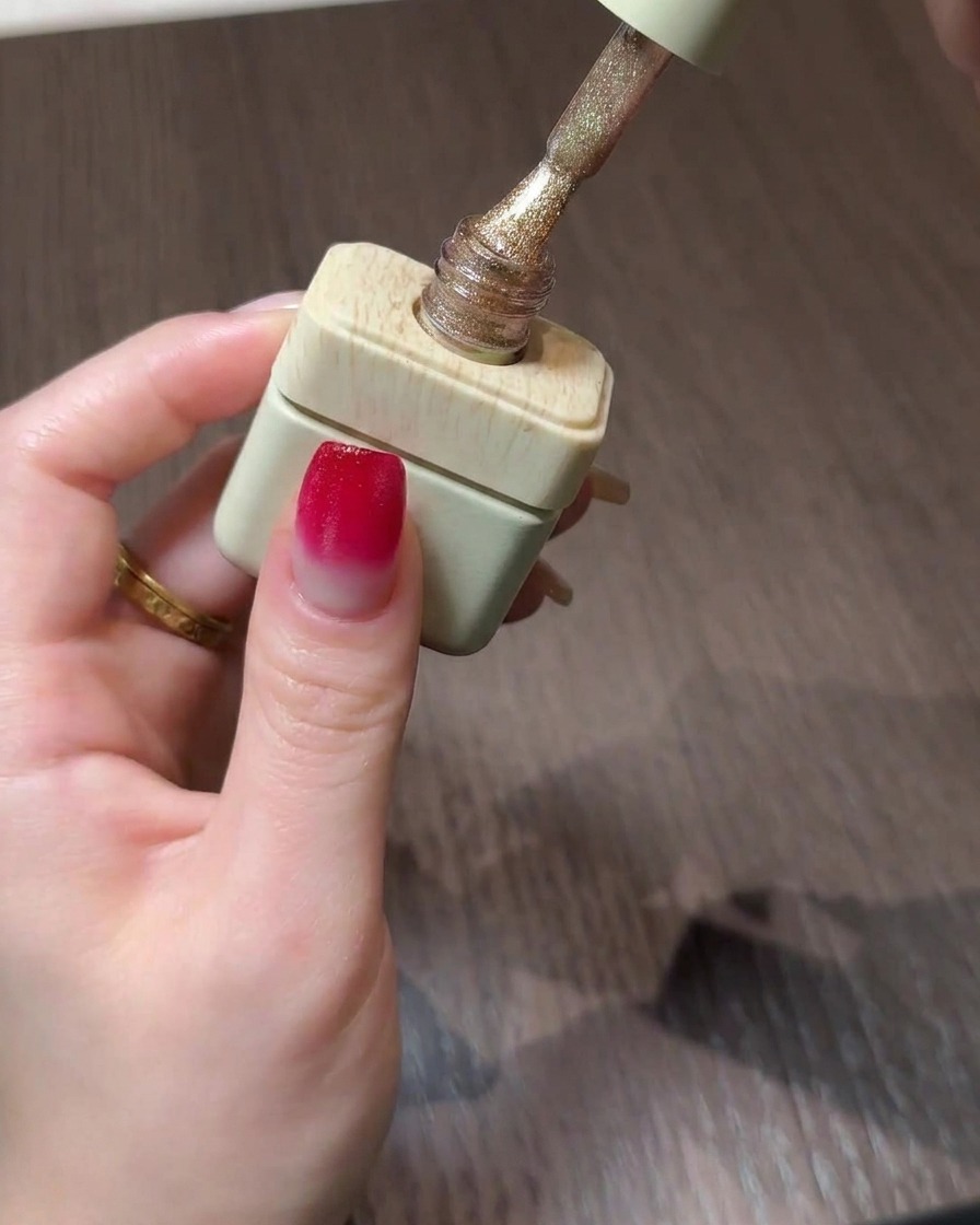 A bottle of gold cat eye gel polish with its brush poised above a gradient nail.