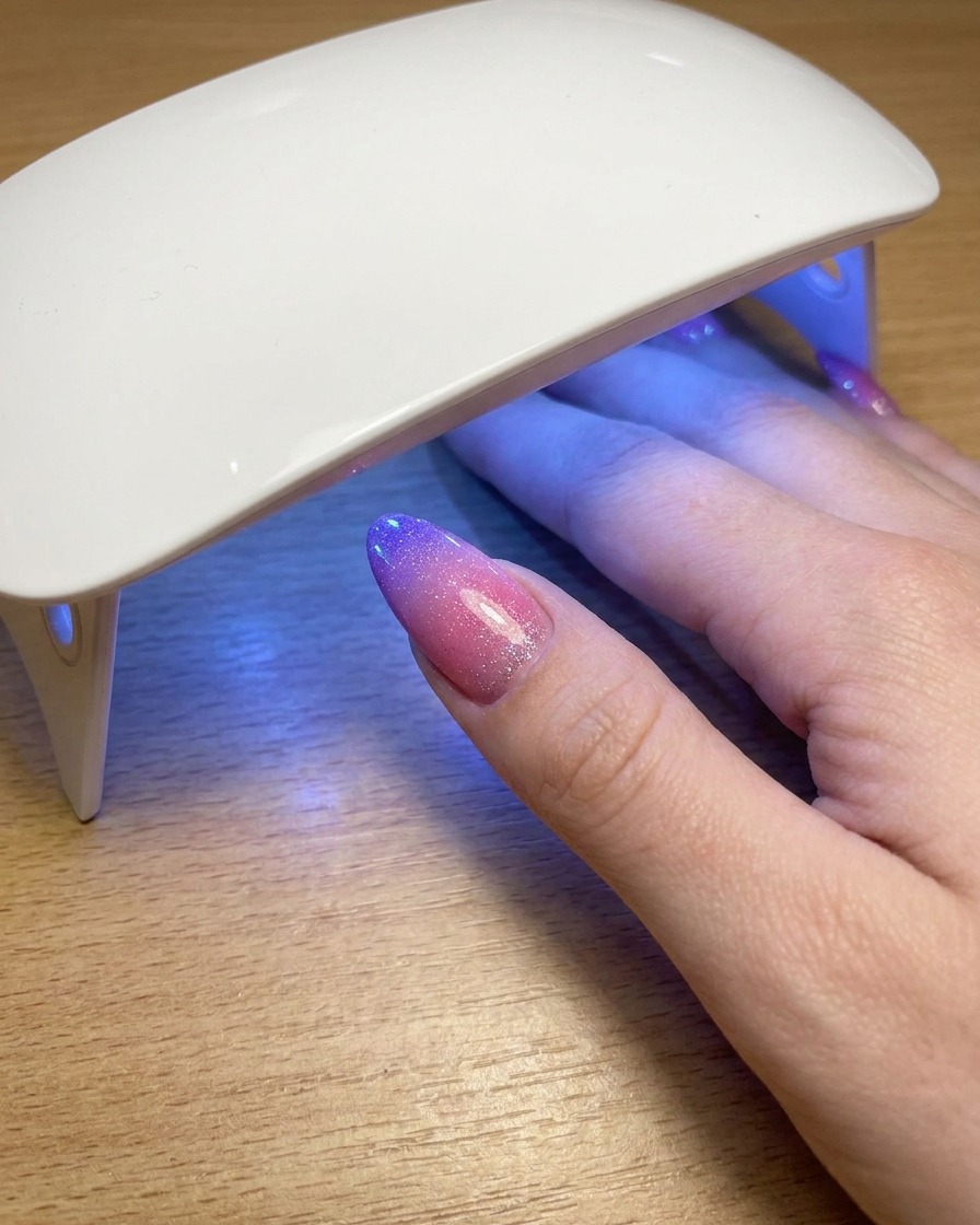 A thumb resting underneath a portable UV lamp while curing the final layer of cat eye gel polish.