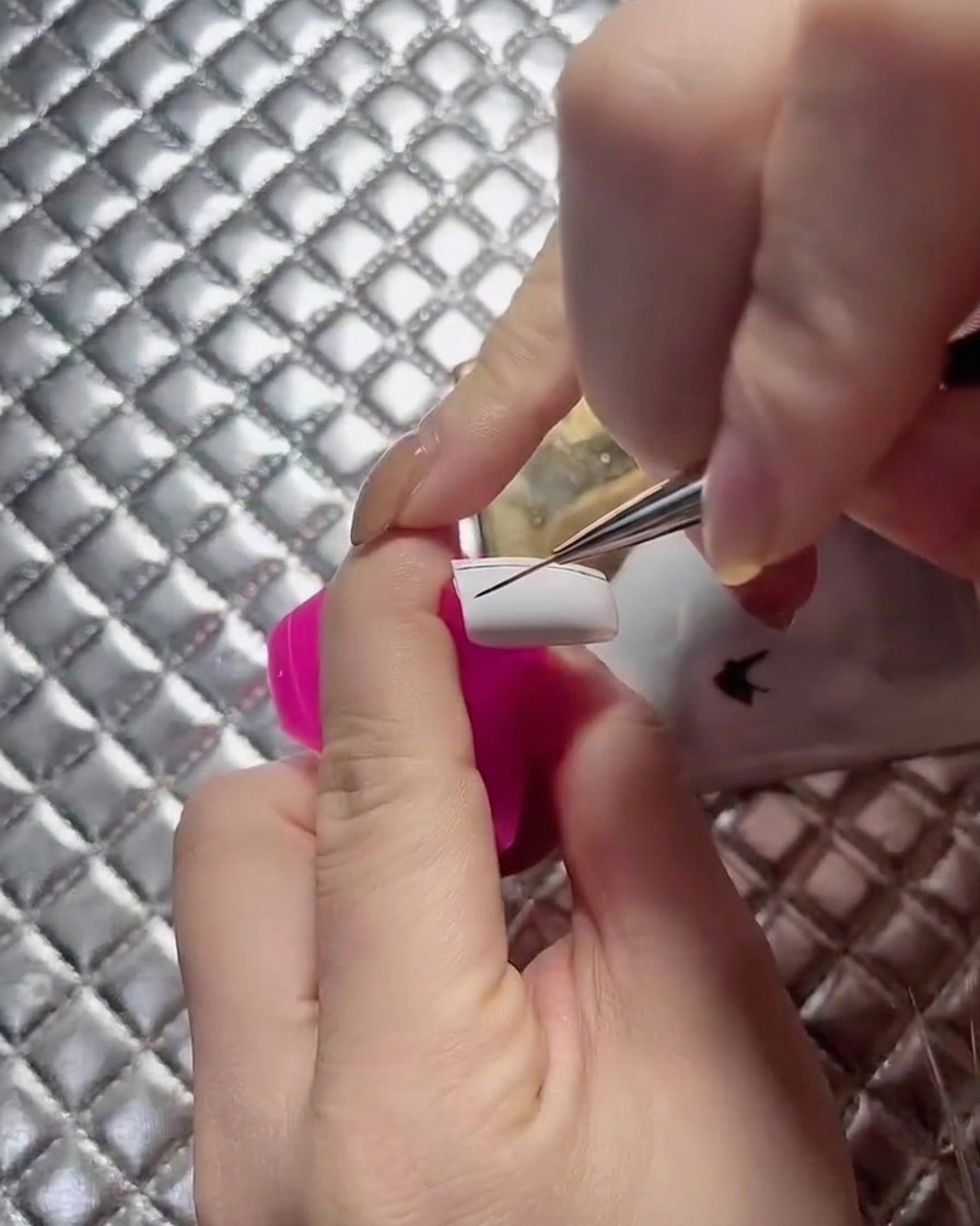 A close-up view of a nail technician extending grid lines across a white nail plate.