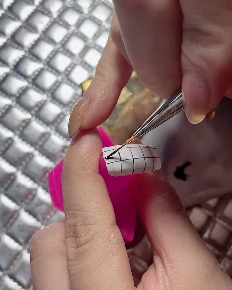 A detail brush neatly coloring alternate squares on a grid-patterned nail.