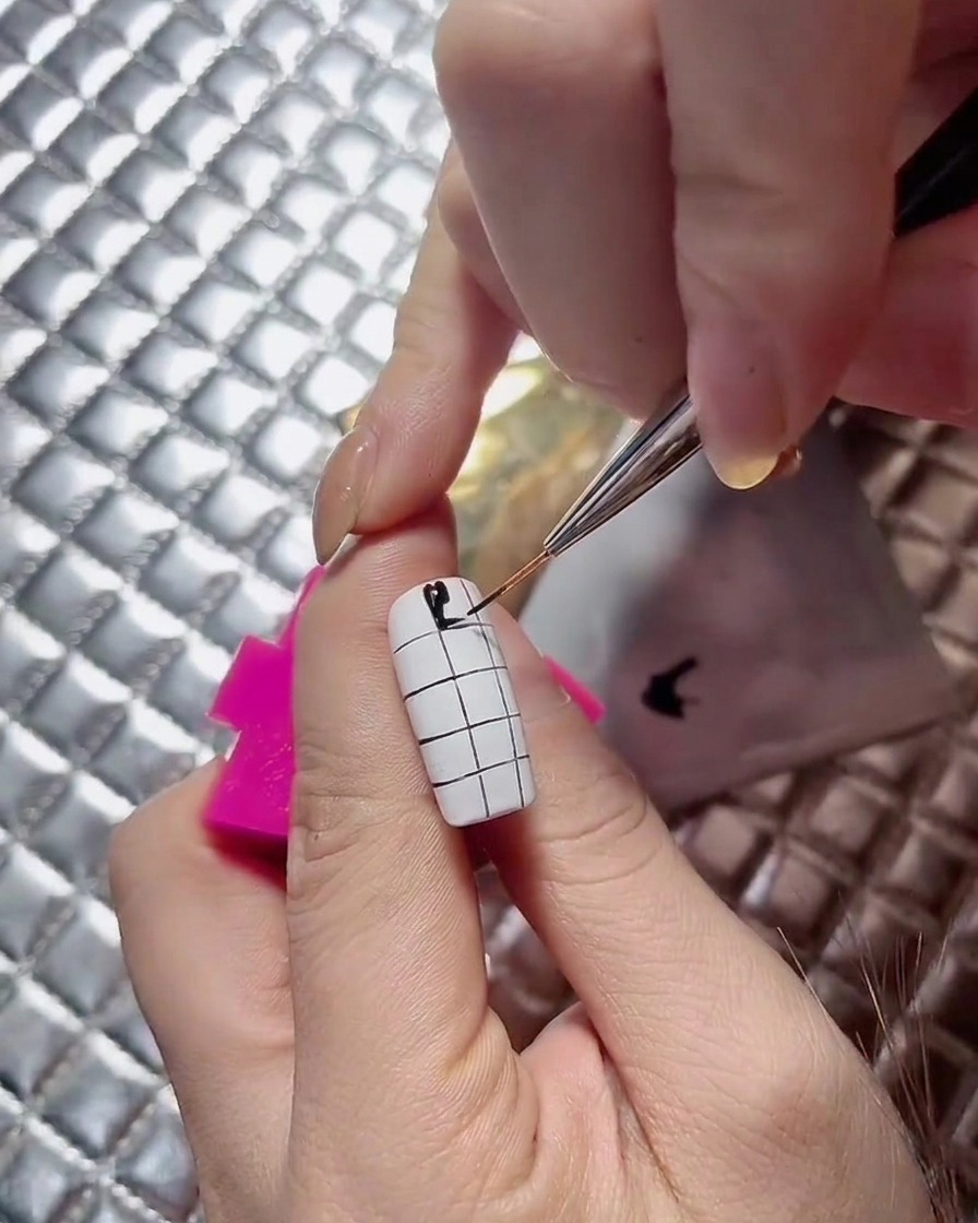 A nail artist continuing the alternating black squares down a checkerboard nail design.