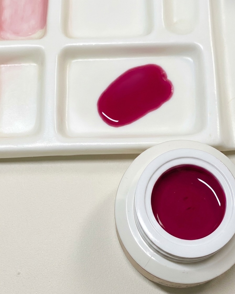 A mixing palette showing a swatch of custom dark pink gel polish next to an open jar of dragon fruit red gel.