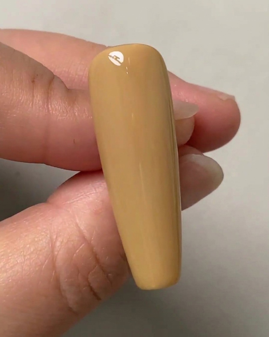 A hand holding a nude-colored practice nail with three faint dots marked vertically down the center.