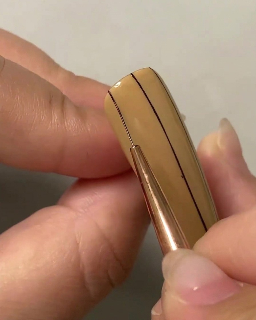 A liner brush drawing a second parallel vertical line on the left side of the nail.