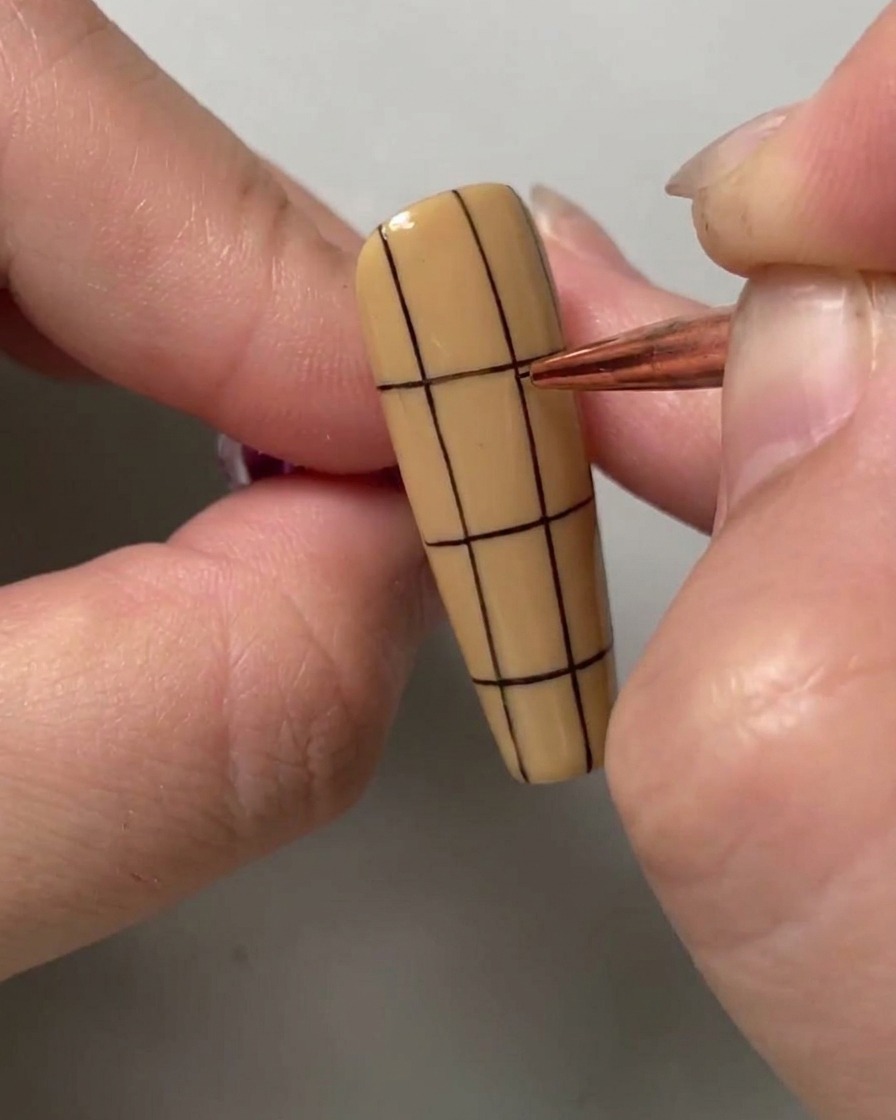 A nail art brush drawing a horizontal black line across the upper half of a vertically striped nail.