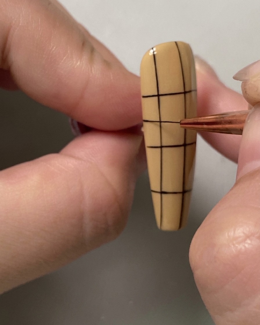 A fine liner brush adding an additional horizontal line to the upper portion of a grid pattern on a nail.