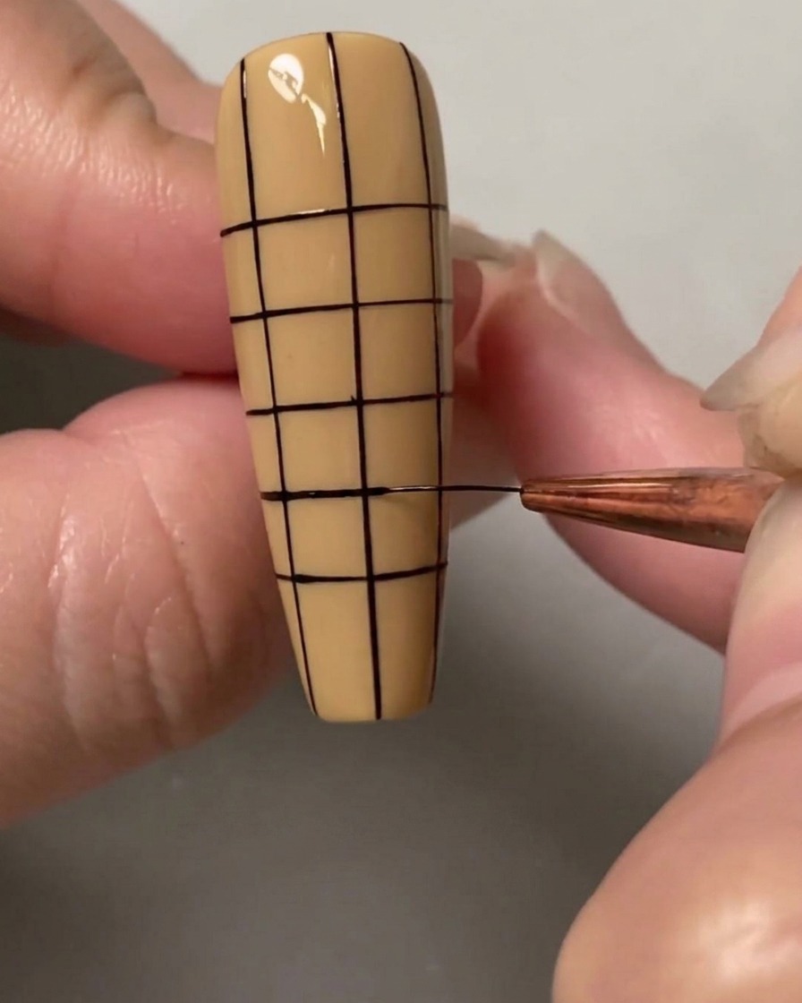 A nail art brush drawing the final horizontal lines to complete a small, even square grid over the entire nail.