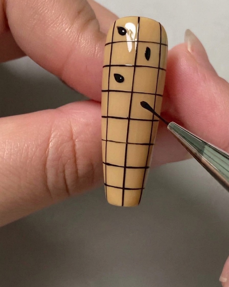 A dotting tool or brush placing small black dots in alternating squares of a grid on a nail.