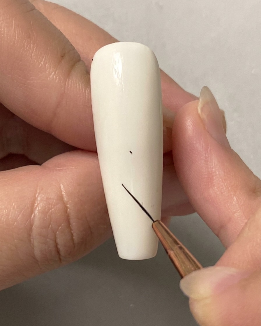 A hand using a fine liner brush to place a tiny dot on a solid white nail.