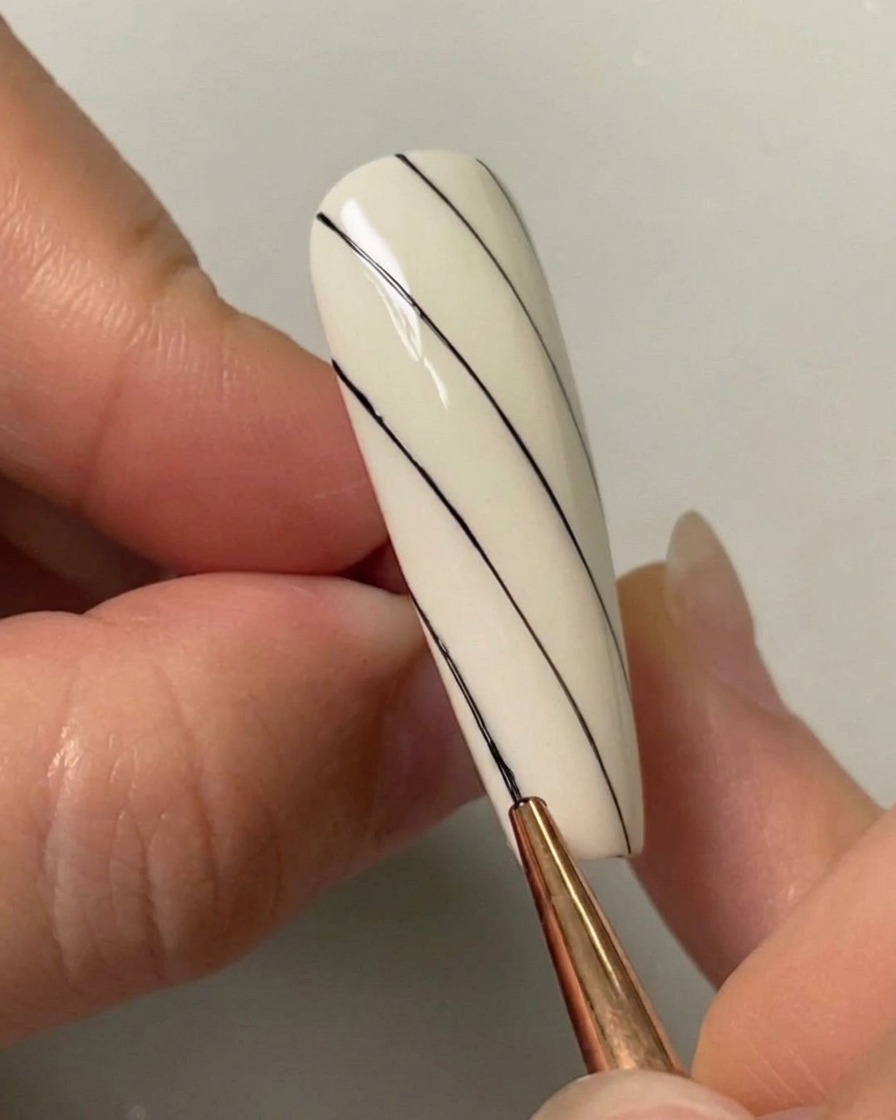 A nail art brush drawing a third diagonal black line on the lower left side of a painted white nail.