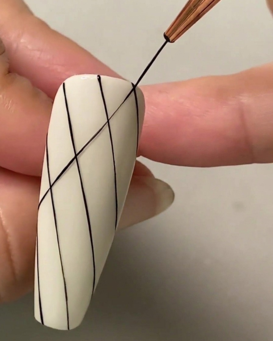 A fine liner brush drawing an intersecting diagonal black line across existing parallel lines to form a diamond grid pattern.