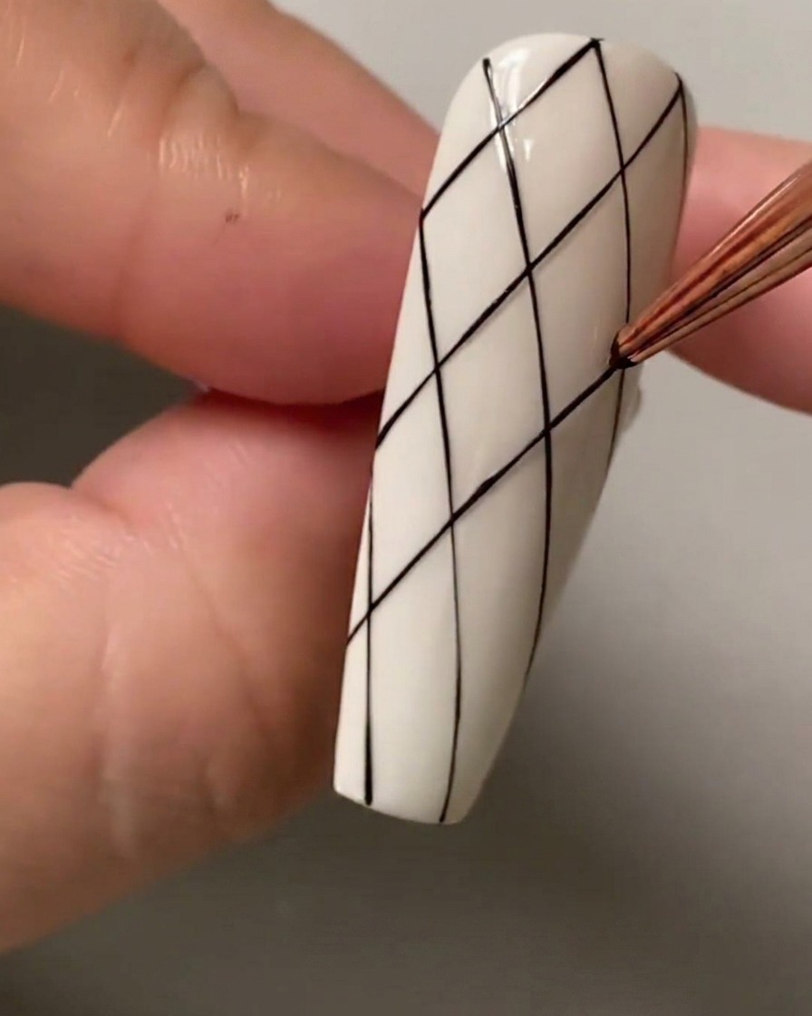 A close-up of a liner brush marking spacing dots on the top section of the nail.