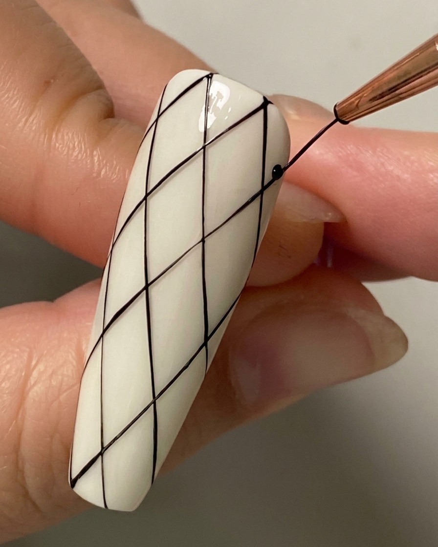 A close-up of a liner brush drawing an intersecting diagonal line on the lower half of the nail.