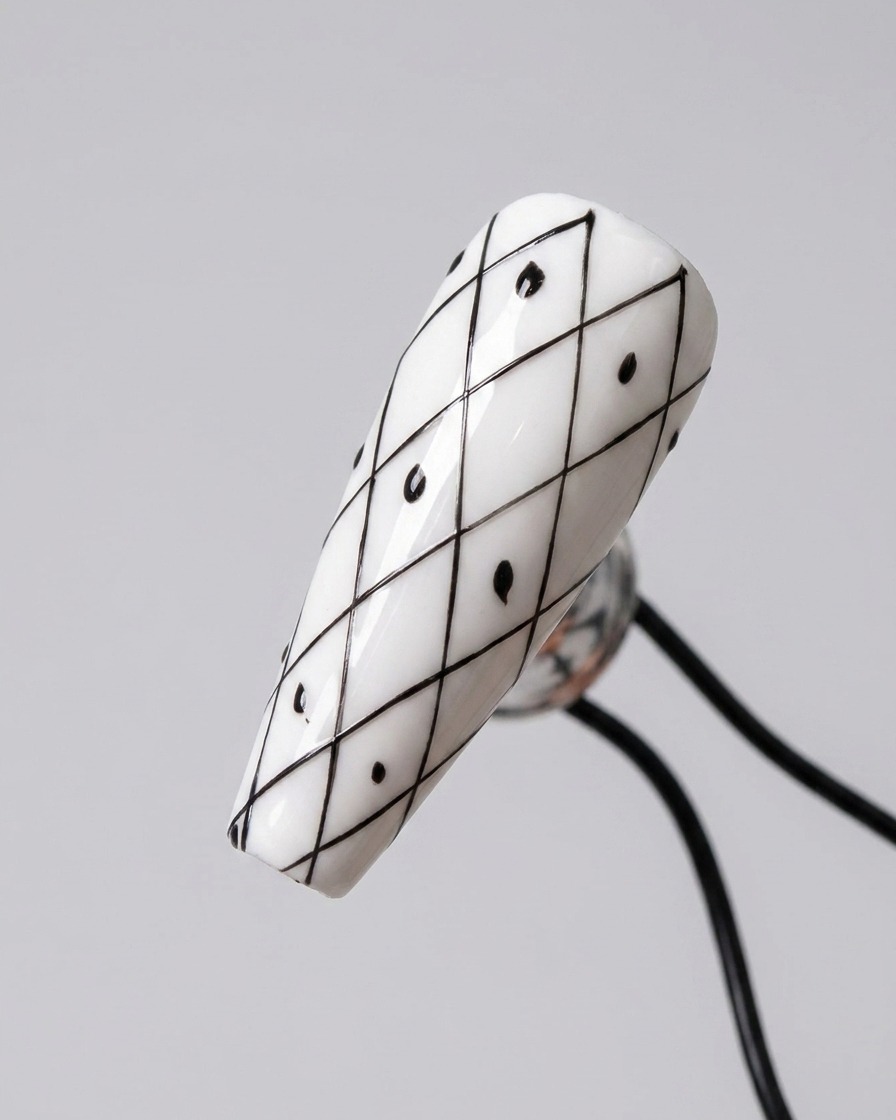 A nail with a black diamond grid pattern featuring small black dots placed inside alternating diamond shapes.