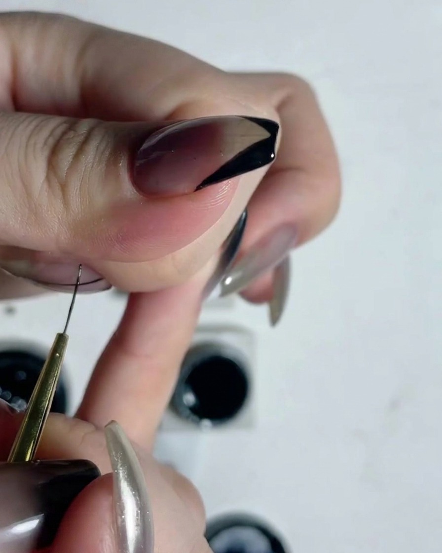 A close-up view of a fine liner brush drawing precise vertical lines on a translucent nail.