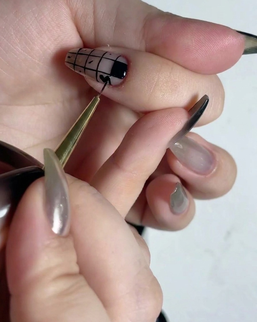 A fine detailing brush filling in alternate squares of a grid pattern on a nail with black polish.