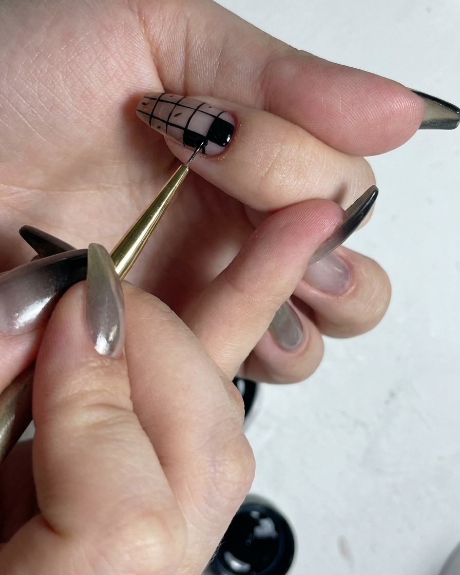 A fine brush touching up the edges of filled black squares in a checkered nail art design to make them crisp.
