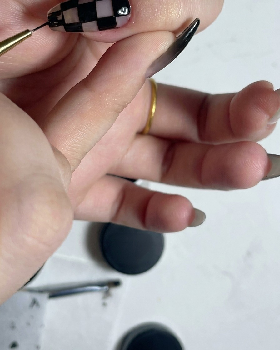 A fine liner brush outlining the perimeter of a completed black and white checkered nail pattern.