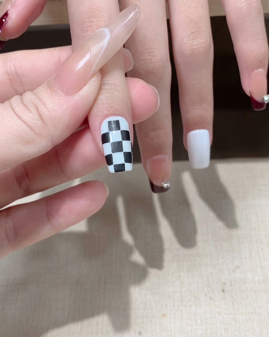 A brush applying a glossy top coat over a completed black and white checkered nail design.