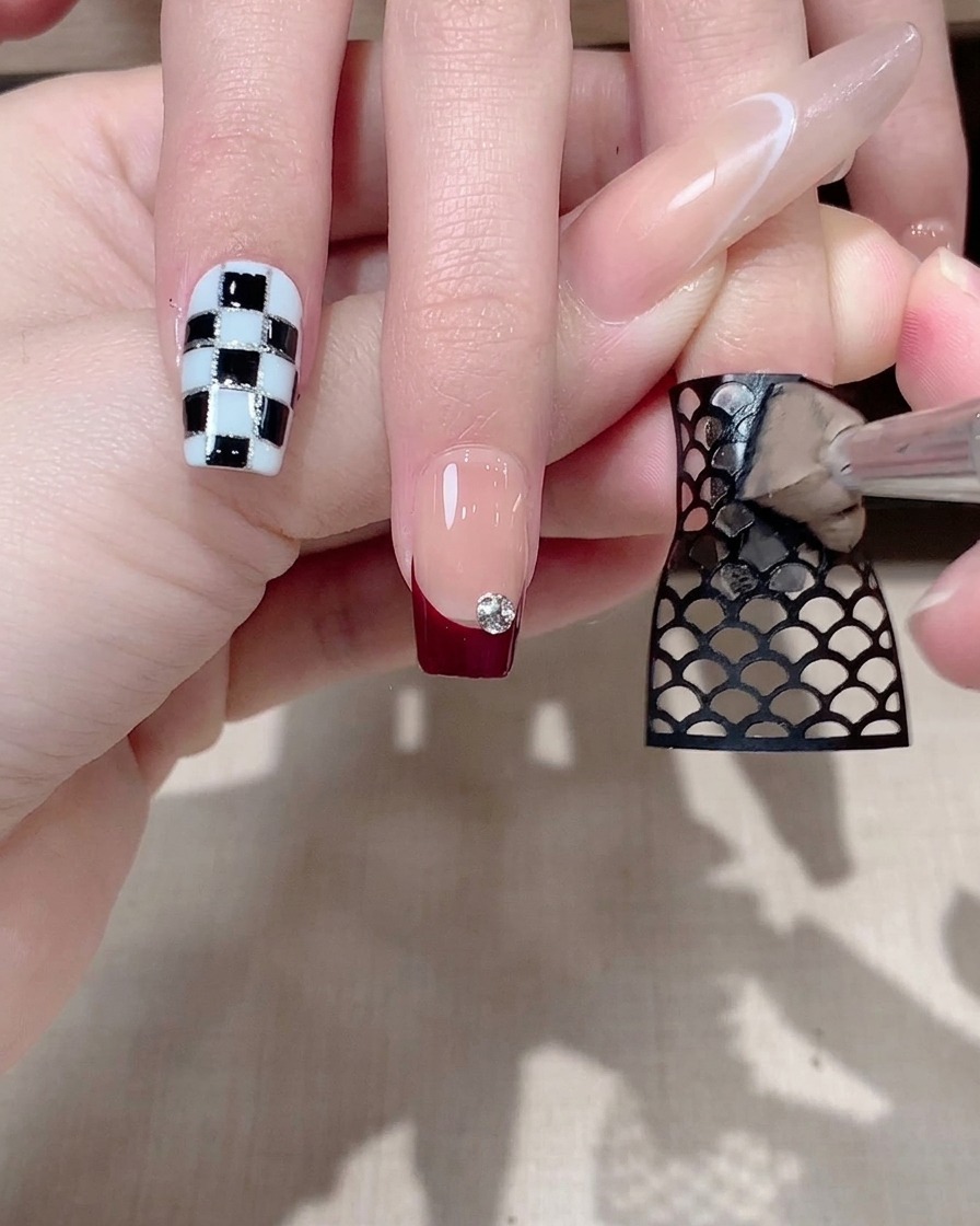 Tweezers gently peeling away a black mesh sticker from a fingernail, revealing a pattern underneath.
