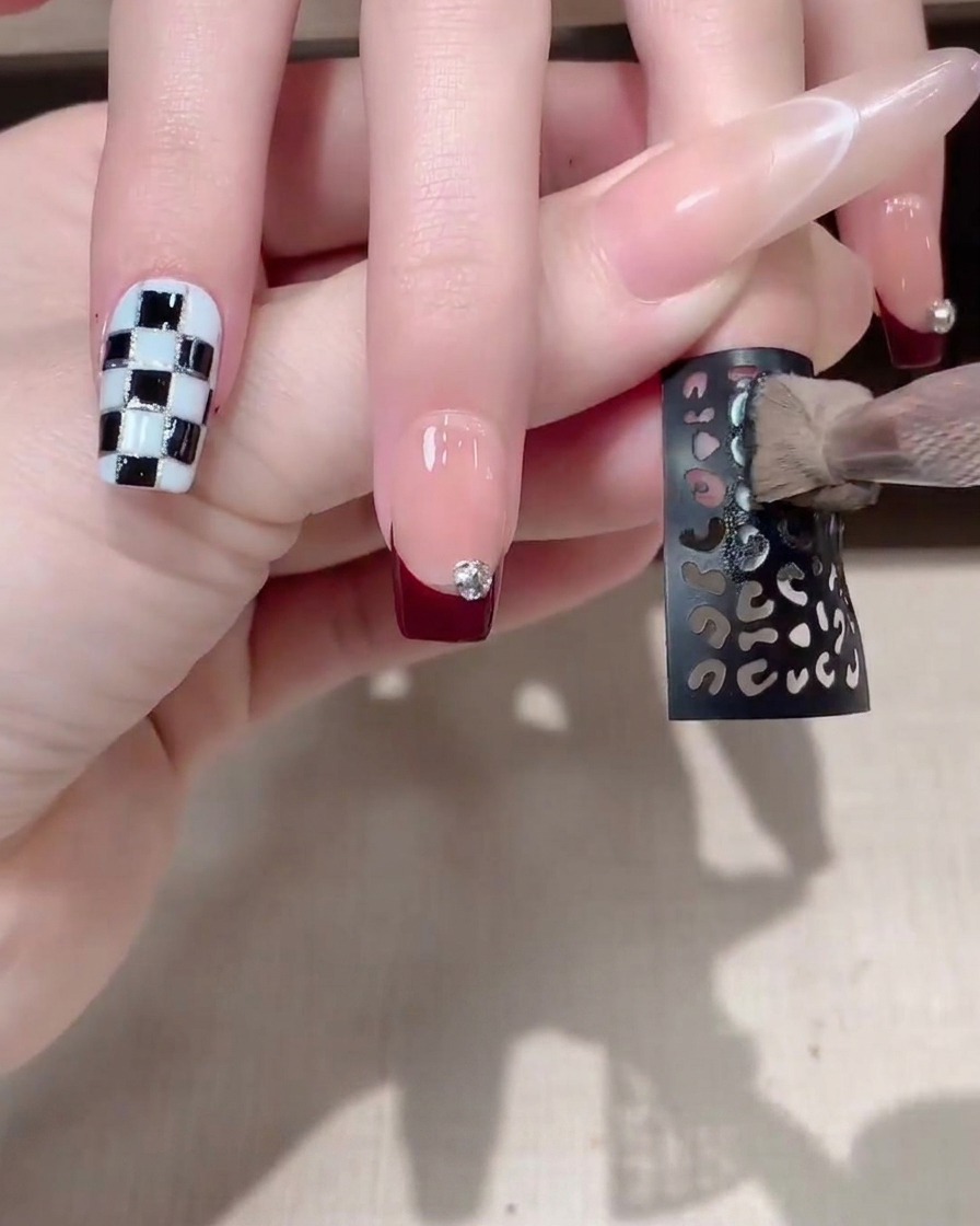 A dark hollow pattern sticker being applied onto a manicured fingernail.