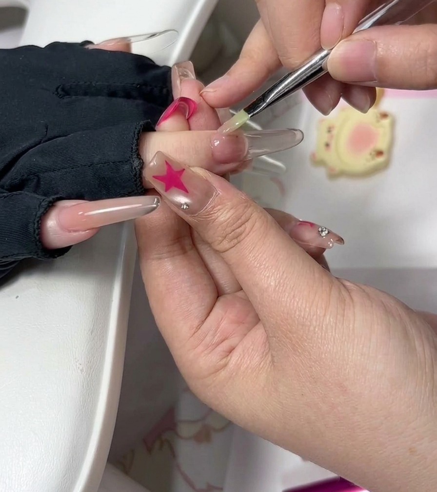 A nail technician using a fine brush to carefully smooth gel near the cuticle on an extended nail.