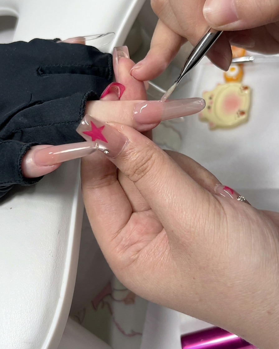 A close-up view of a precision tool and small sponge cleaning around the side of a prepped fingernail.