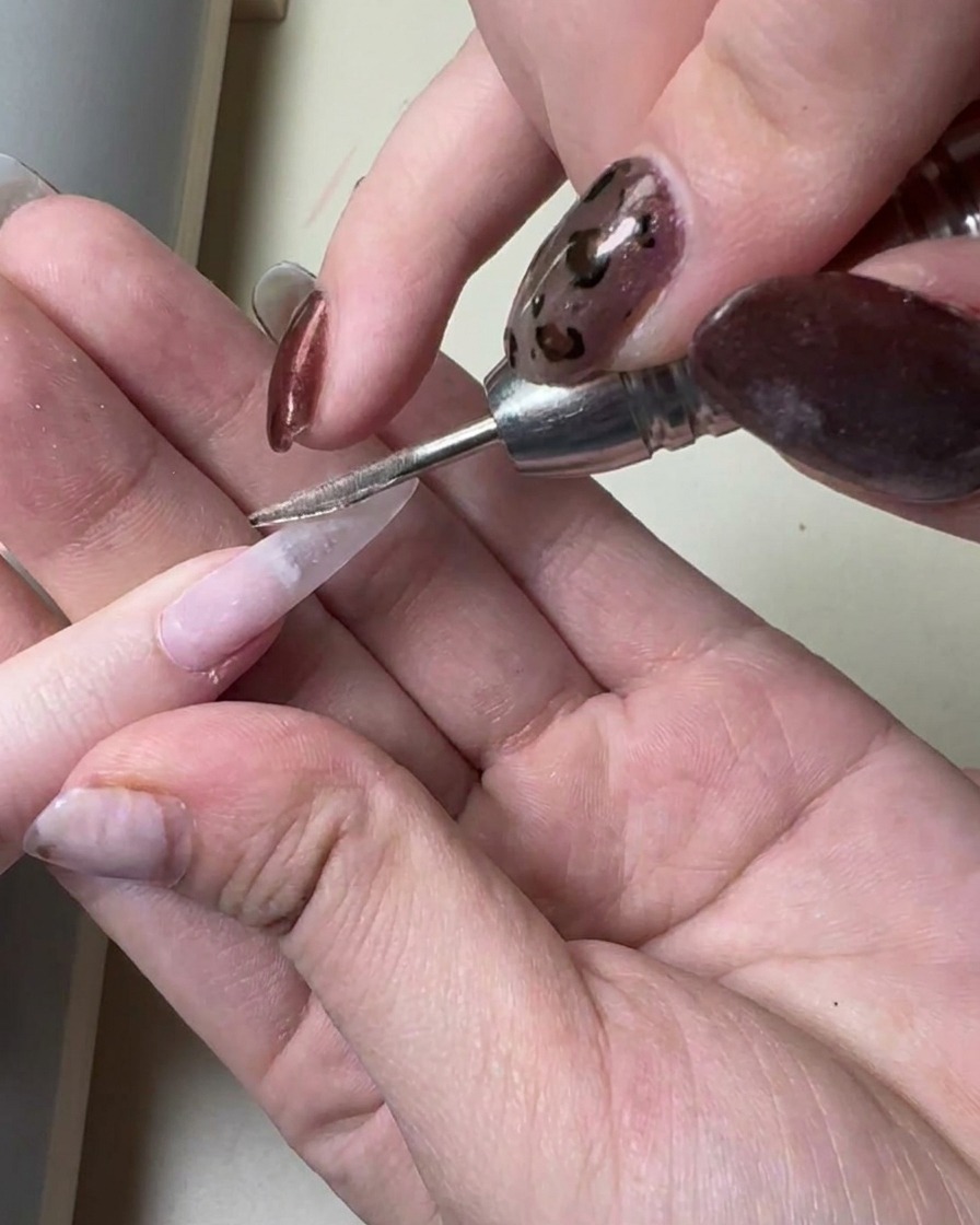 A nail brush applying a thin layer of translucent gray gel onto a long prepped nail extension.