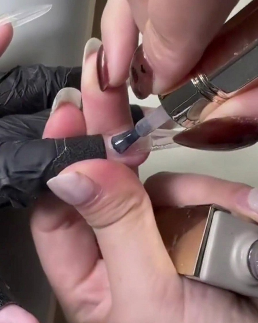 A close-up view of a brush applying light pink translucent gel over the nail extension.