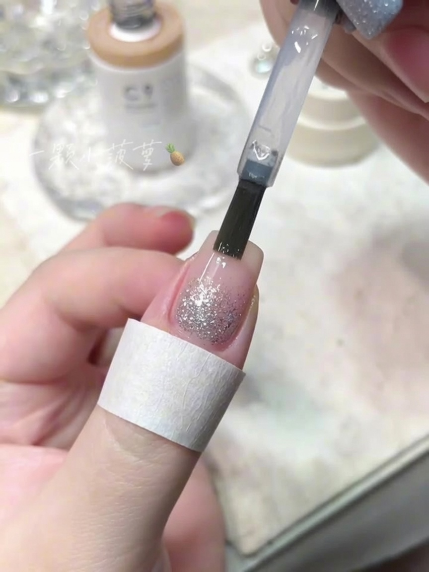 A bottle brush applying a clear top coat over a nail with crushed diamond glitter.