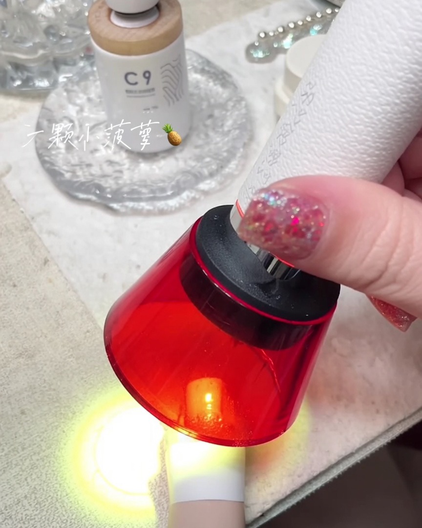 A handheld red mini UV lamp curing a nail on a finger.