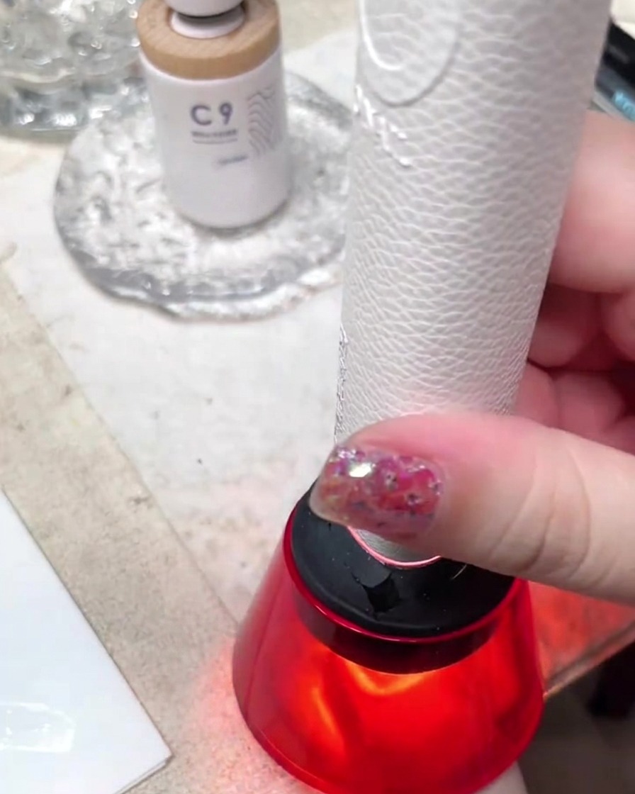 A compact handheld red mini UV/LED lamp curing a nail design in a well-lit studio workspace.