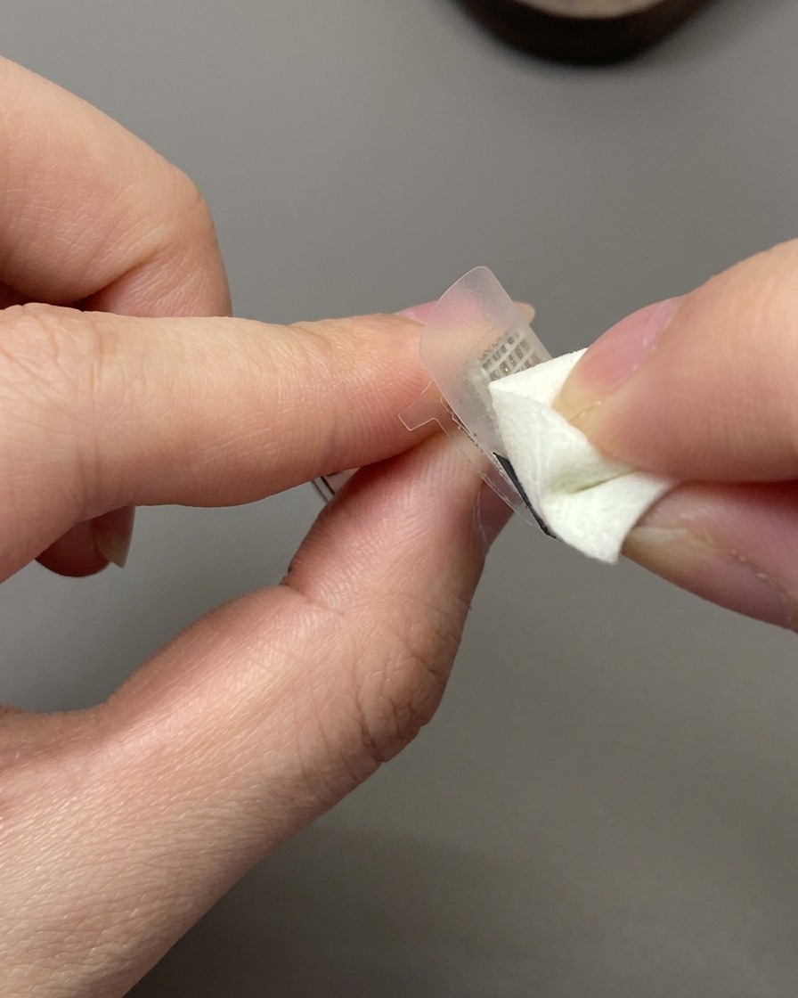 A cosmetic sponge dabbing off-white gel polish onto a French guide sticker on a nail.