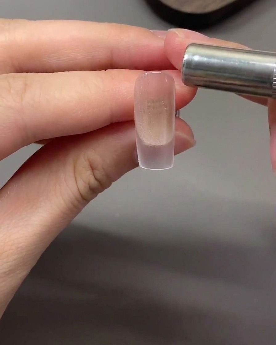 A cylindrical magnet held horizontally near the nail tip to pull magnetic cat eye particles into a light band.