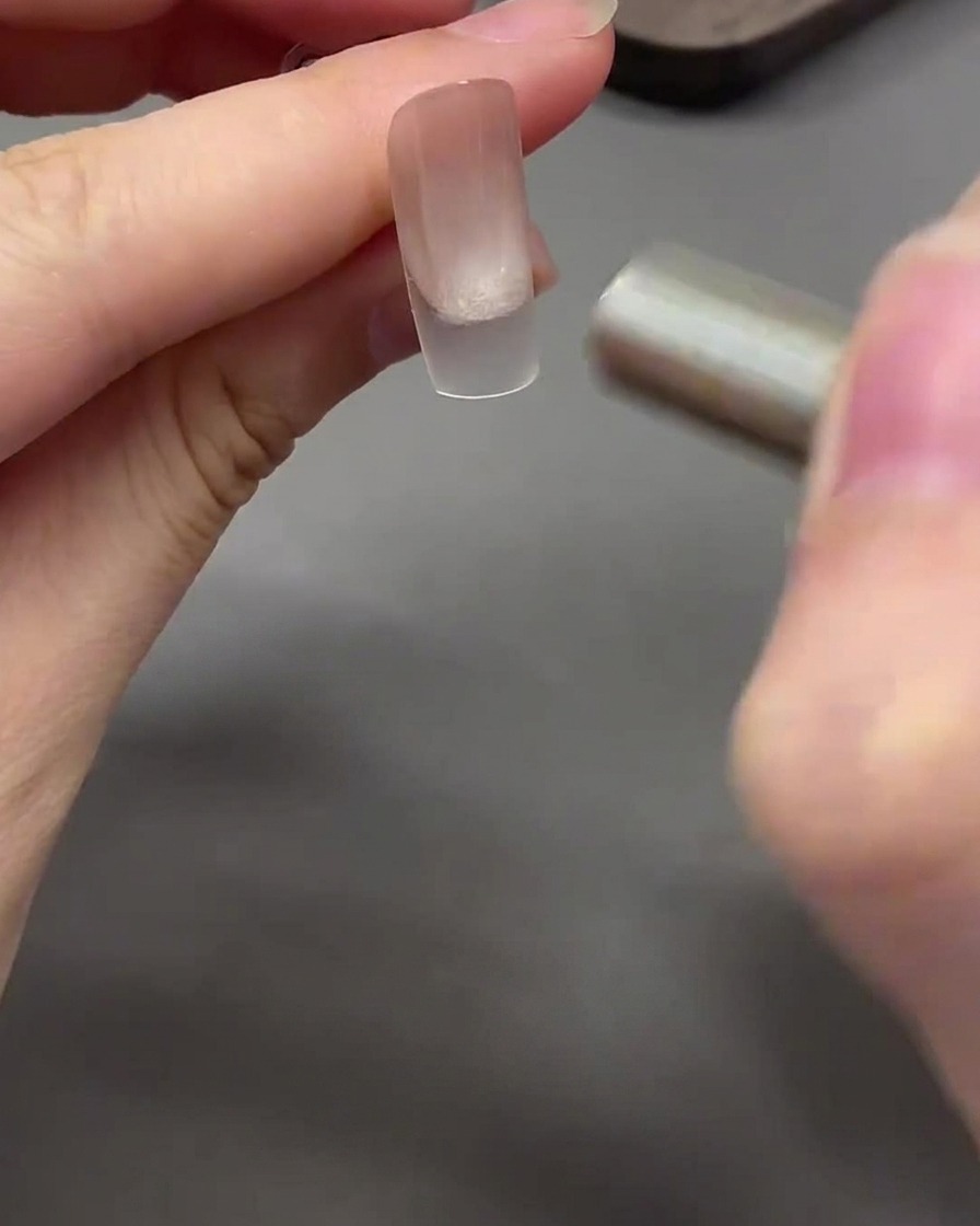 A magnet moving in a curved motion around the nail tip to shape the cat eye gel into a glass bead effect.