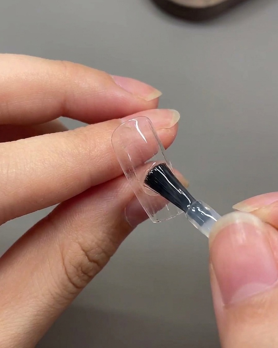 A brush applying a layer of matte top coat across the entire surface of the nail.