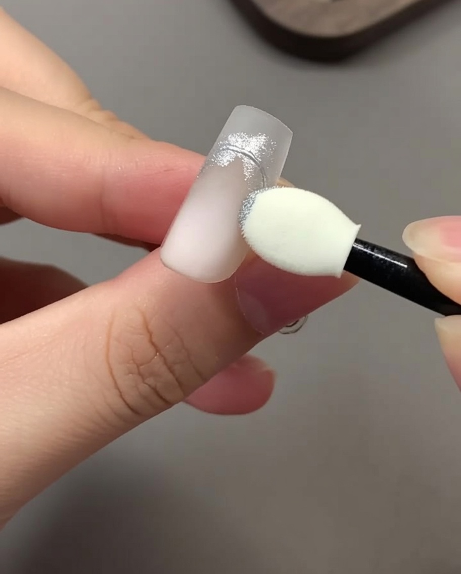 An eyeshadow sponge applicator rubbing silver chrome powder onto a nail design.