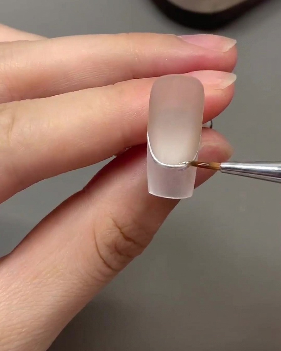 A liner brush applying a protective layer of clear reinforcement gel over a silver chrome line.