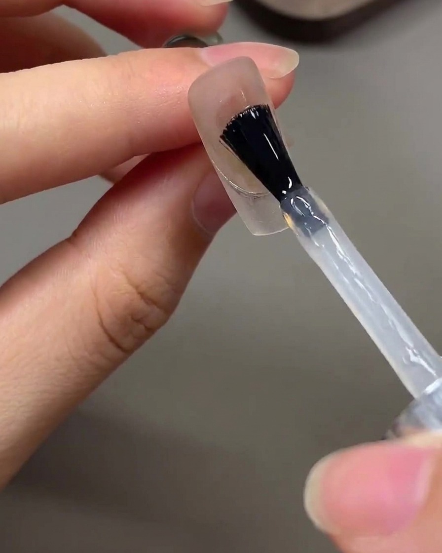 A brush applying a clear glossy top coat over a finished nail design.