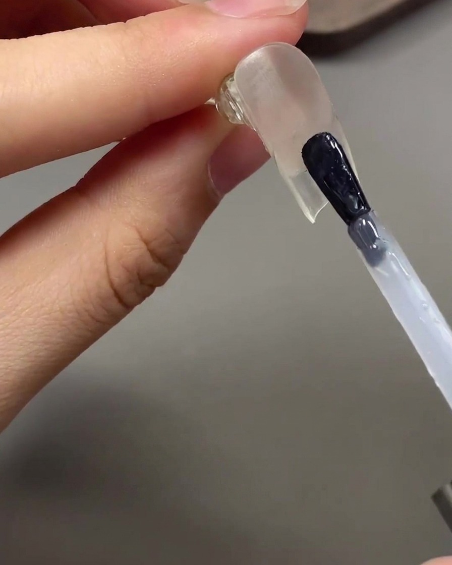 A brush applying clear glossy top coat underneath the extended nail tip.