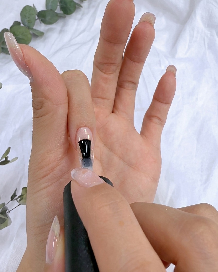 A brush applying clear reinforcing gel over a natural nail surface.