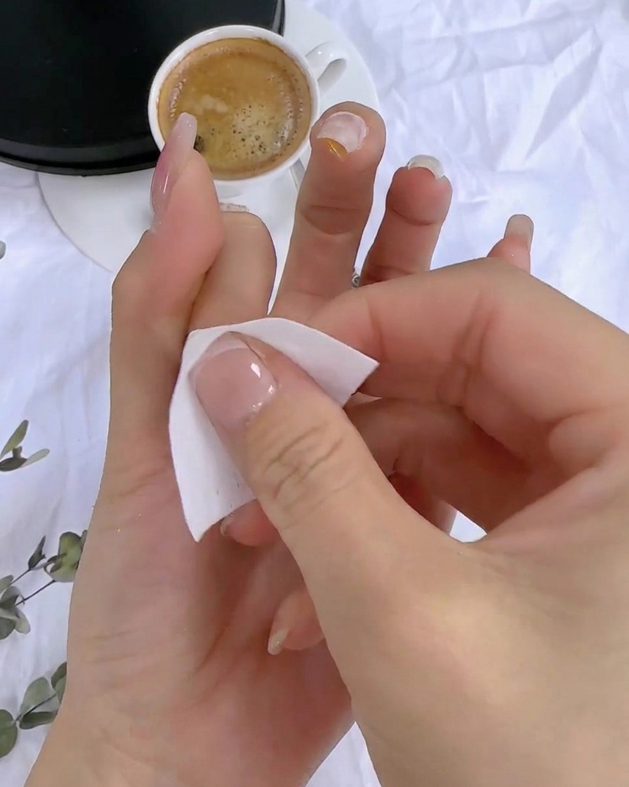 A hand using a lint-free wipe to clean the sticky residue off the cured nail surface.