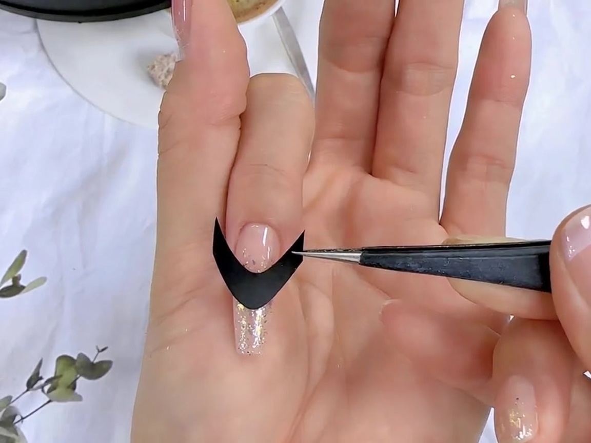 A pair of tweezers placing a black French guide sticker onto a prepped nail surface.