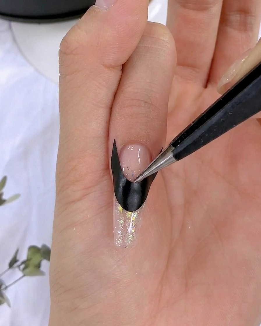 Tweezers smoothing down a black French sticker on a nail.