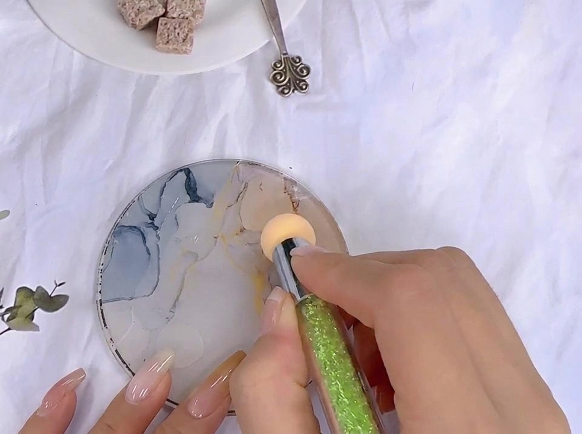 A sponge tool dabbing into color gel spread out on a patterned glass mixing palette.