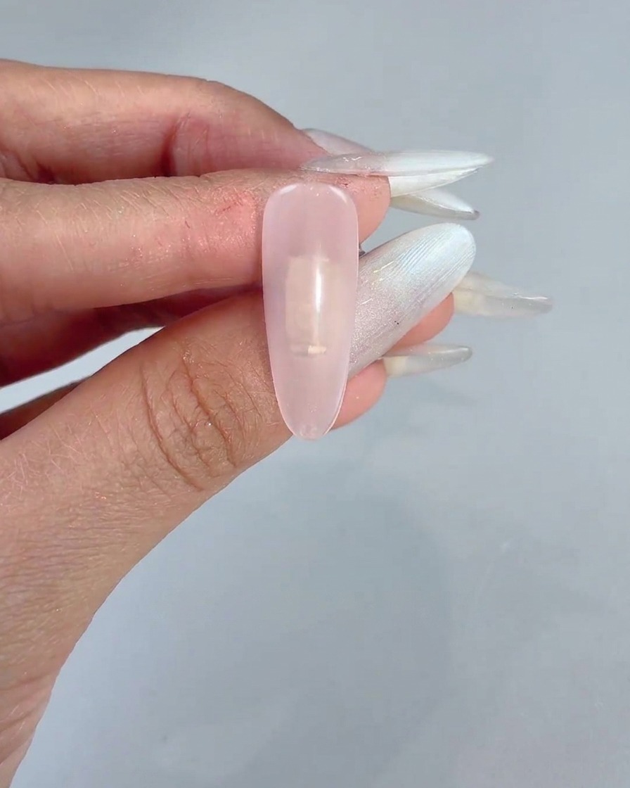 A sponge block dabbing gentle pink gel onto the center of a clear manicured nail.