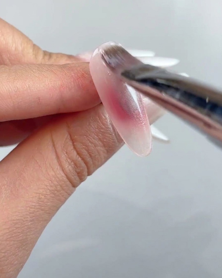 A nail brush applying a coat of clear cat-eye gel over the entire surface of the prepared nail.